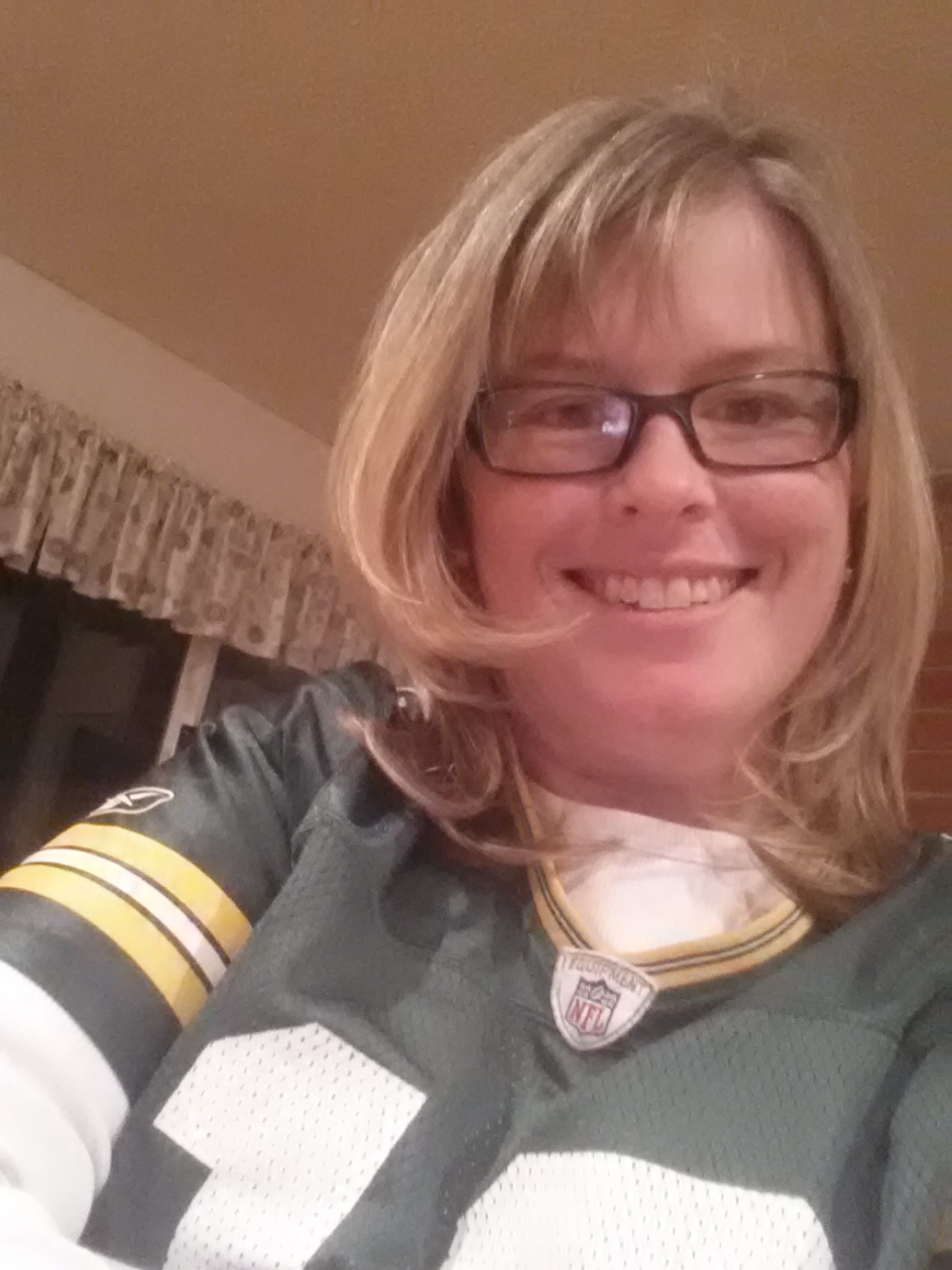 A white woman with brown, rectangular glasses, blonde hair, and a Green Bay Packers jersey